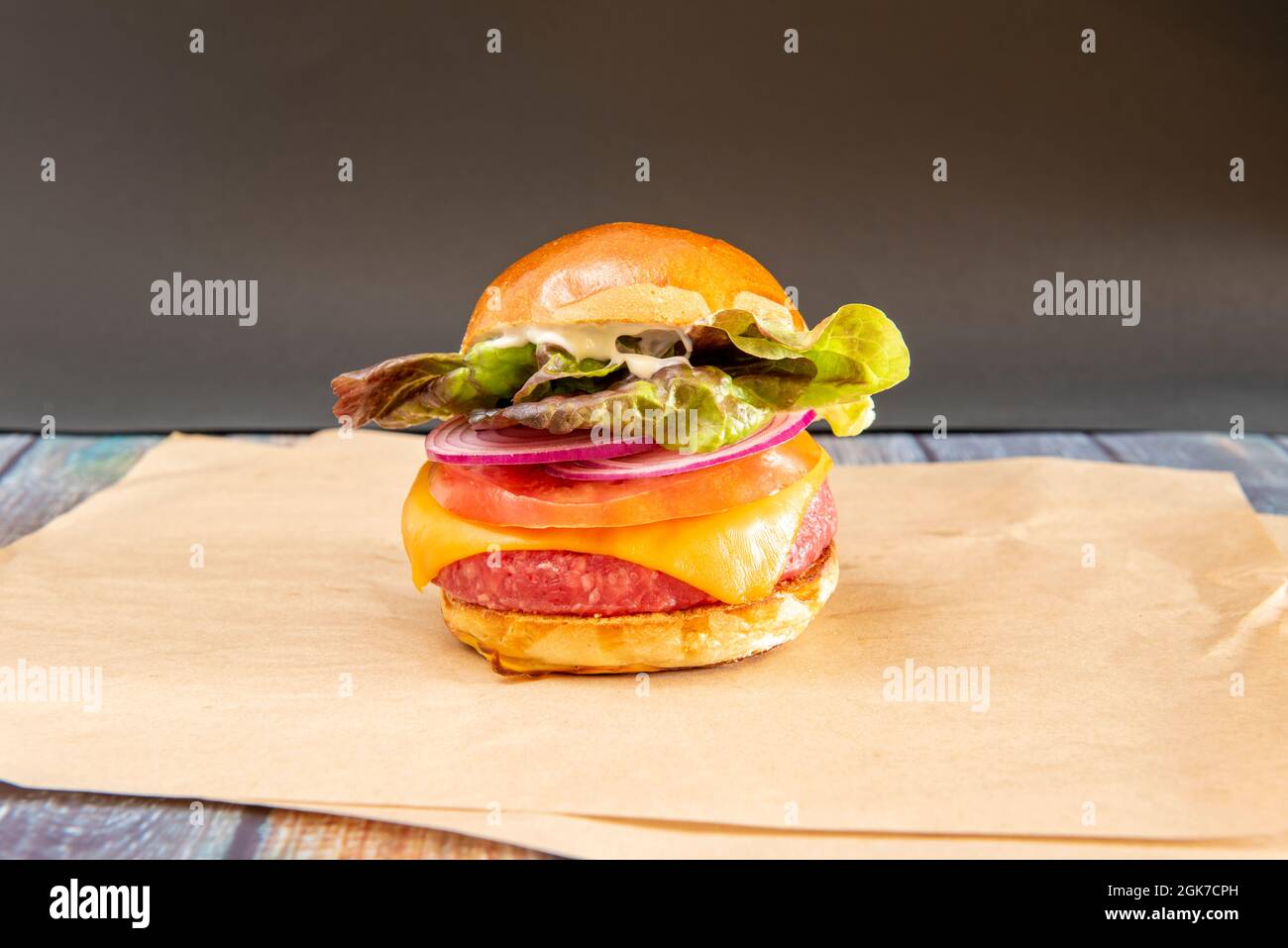 Hamburger di manzo vegano con formaggio cheddar, cipolla rossa cruda, lattuga e maionese su carta greaseproof Foto Stock