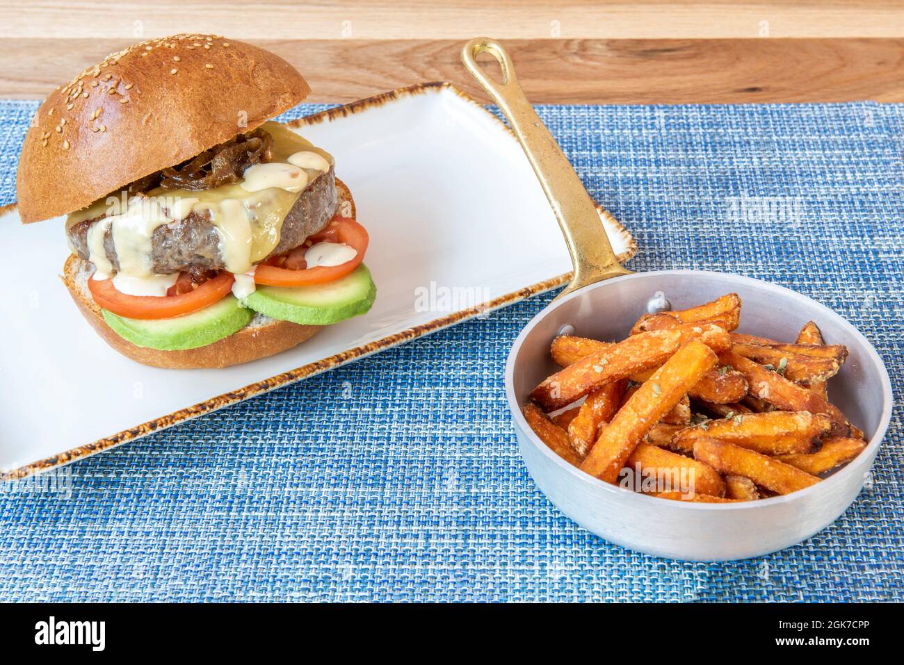 Hamburger di manzo con cipolla caramellata e avocado guarnito con patate dolci su tovaglia blu Foto Stock