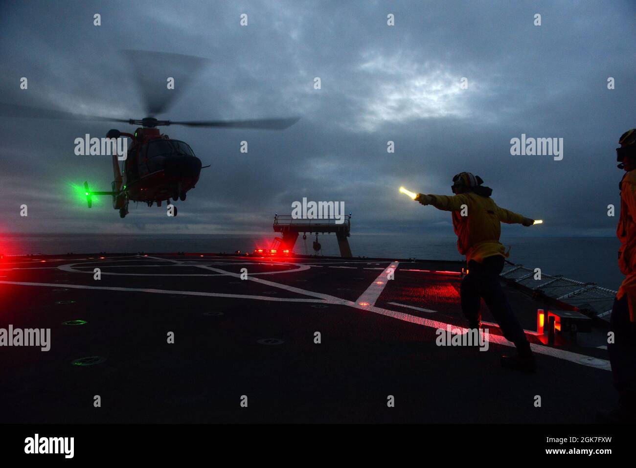 ENS. Ryan Dunkle, membro dell'equipaggio della Guardia Costiera Cutter Healy (WAGB 20), trasmette i segnali di atterraggio ai piloti di Air Station Kodiak che volano su un elicottero MH-65 Dolphin durante le operazioni di addestramento notturno al largo della costa dell'Alaska durante lo spiegamento artico di Healy il 25 agosto 2021. Gli addetti al segnale di atterraggio sono responsabili della comunicazione con l'equipaggio e i membri dell'equipaggio di taglio durante le operazioni di volo. Foto Stock