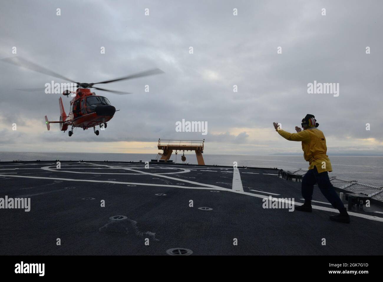 ENS. Ryan Dunkle, membro dell'equipaggio della Guardia Costiera Cutter Healy (WAGB 20), trasmette i segnali di atterraggio ai piloti di Air Station Kodiak che volano su un elicottero MH-65 Dolphin durante le operazioni di addestramento congiunto al largo della costa dell'Alaska durante lo spiegamento artico di Healy il 25 agosto 2021. Gli addetti al segnale di atterraggio sono responsabili della comunicazione con l'equipaggio e i membri dell'equipaggio di taglio durante le operazioni di volo. Foto Stock