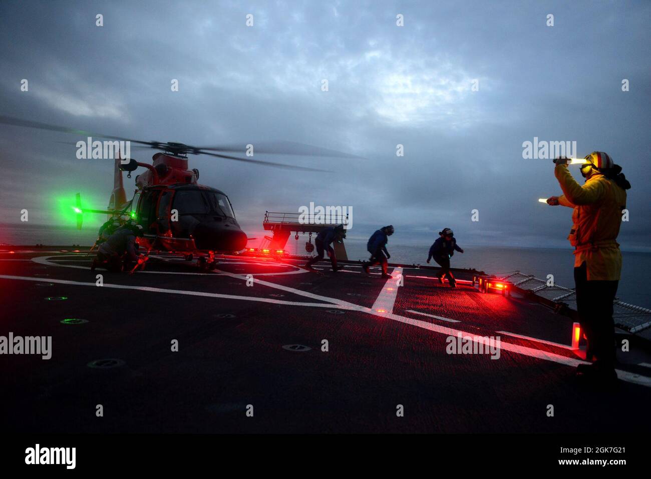 ENS. Ryan Dunkle, membro dell'equipaggio della Guardia Costiera Cutter Healy (WAGB 20), dà comandi a un team di cravatta durante le operazioni notturne di addestramento in volo congiunto con Air Station Kodiak al largo delle coste dell'Alaska durante lo spiegamento artico di Healy il 25 agosto 2021. Gli addetti al segnale di atterraggio sono responsabili della comunicazione con l'equipaggio e i membri dell'equipaggio di taglio durante le operazioni di volo. Foto Stock