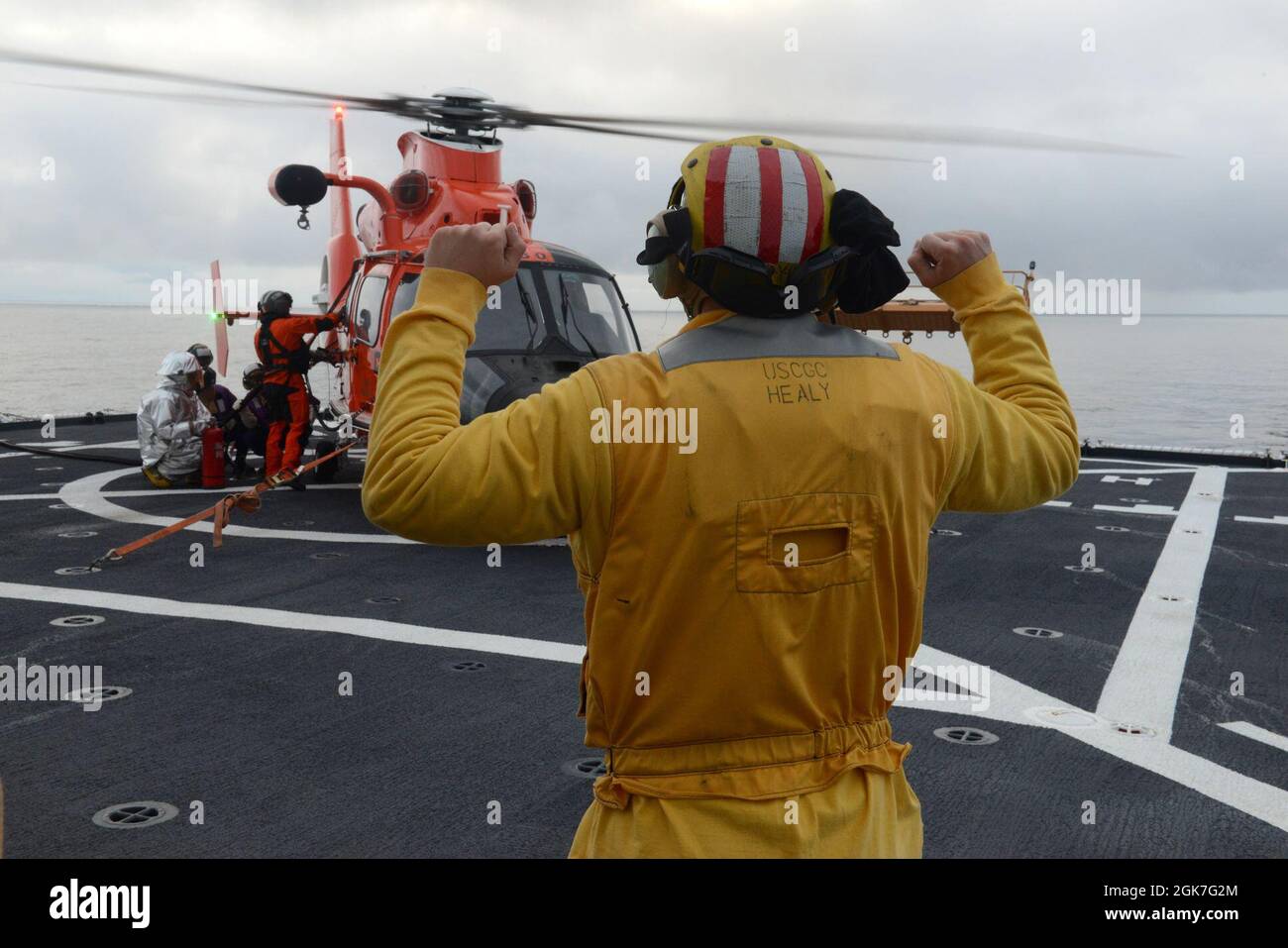 ENS. Ryan Dunkle, membro dell'equipaggio della Guardia Costiera Cutter Healy (WAGB 20), trasmette i segnali a un team di rifornimento mentre rifornisce un elicottero Air Station Kodiak MH-65 Dolphin durante le operazioni di addestramento congiunto al largo della costa dell'Alaska durante lo spiegamento artico di Healy il 25 agosto 2021. Gli addetti al segnale di atterraggio sono responsabili della comunicazione con l'equipaggio e i membri dell'equipaggio di taglio durante le operazioni di volo. Foto Stock
