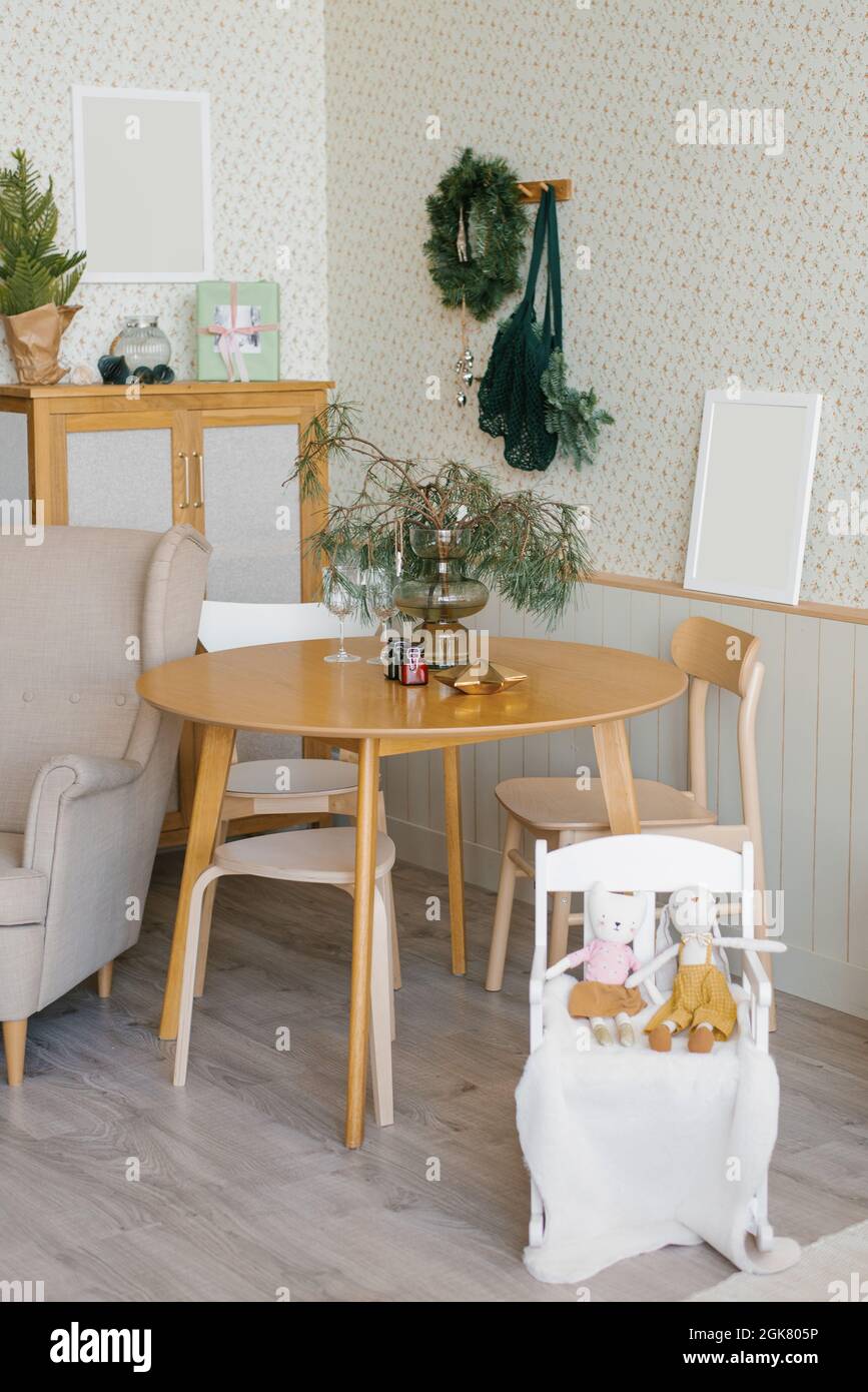 Decorazioni natalizie nel soggiorno in stile scandinavo: Due bicchieri su un tavolo di legno, rami di abete rosso in vaso e candele, una seggiolone con Foto Stock