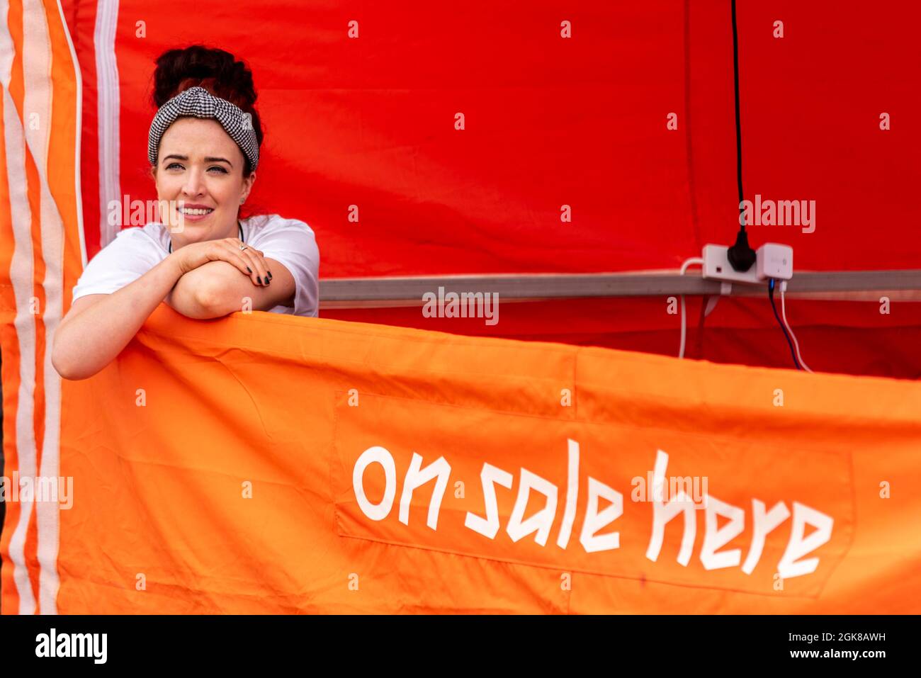 Venditore di merchandising femminile in un festival di concerti musicali a Garon Park, Southend on Sea, Essex, Regno Unito. In attesa dei clienti Foto Stock