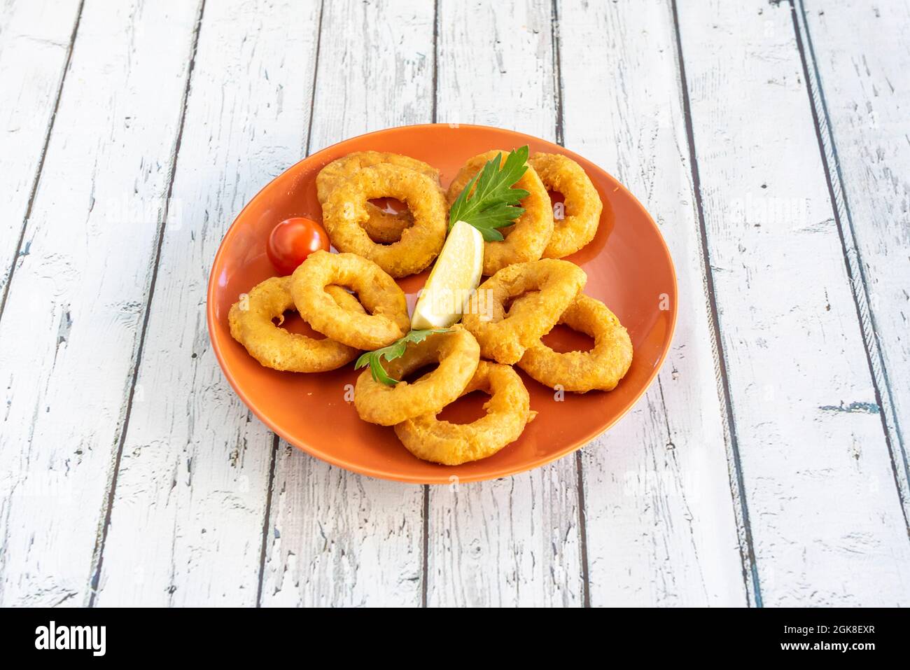 Tapa di calamari lavorati in pastella su piatto arancione con limone e prezzemolo e fondo bianco Foto Stock