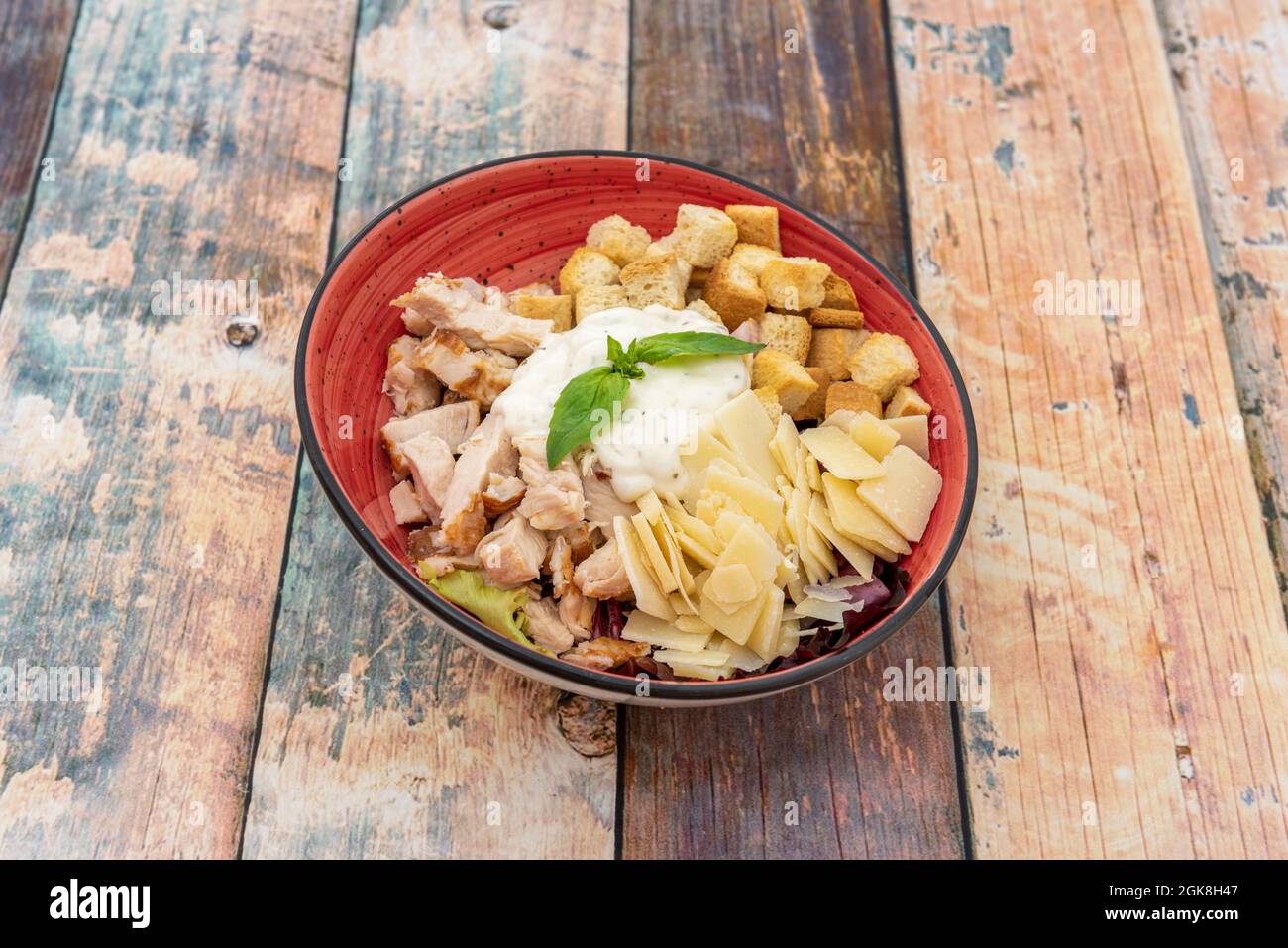 Incredibile insalata caesar con un sacco di parmigiano fiammato, pezzi di  pollo, maionese e crostini all'interno di un recipiente rosso su sfondo di  legno Foto stock - Alamy