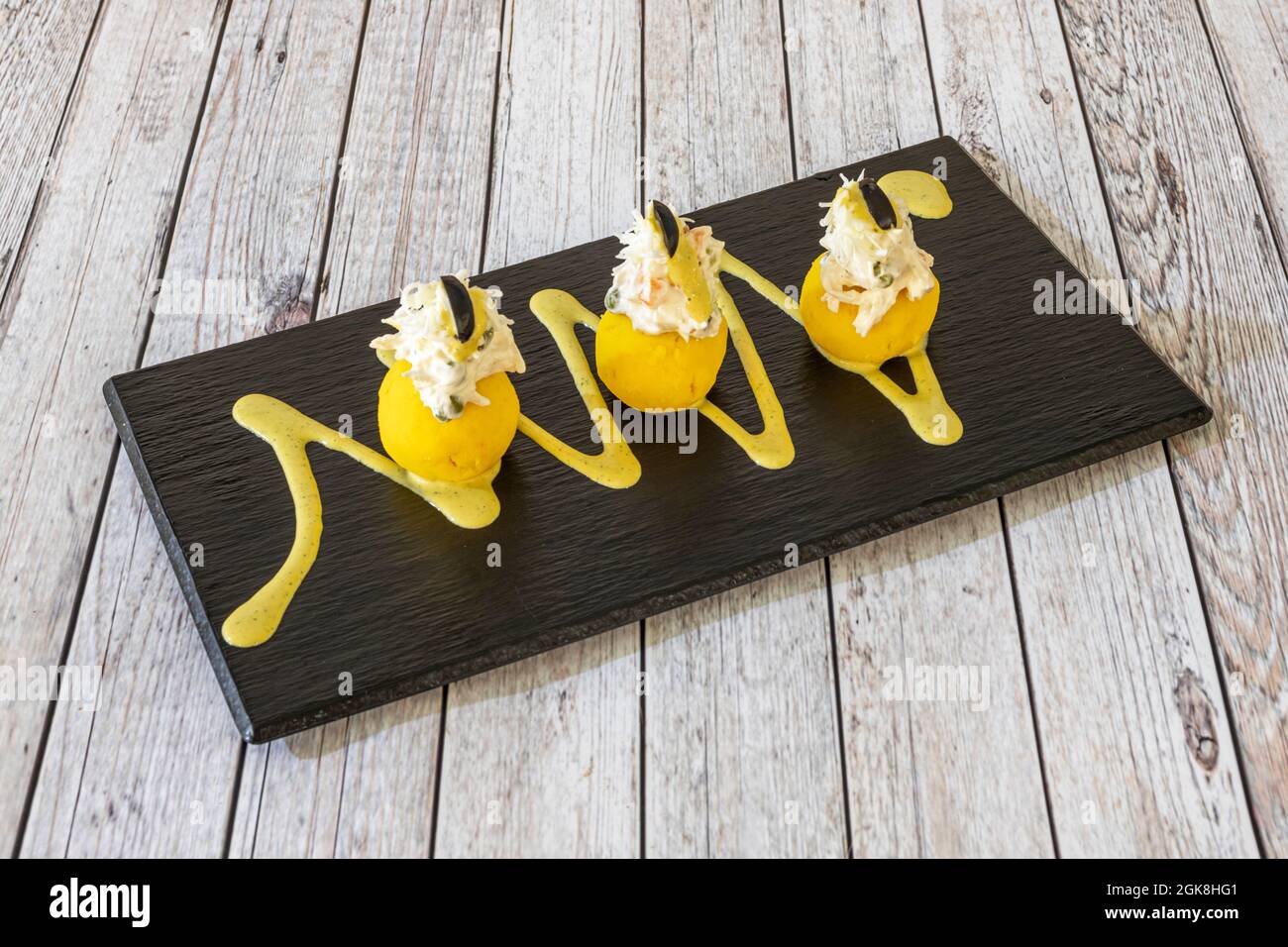 Sandwich di causa da Lima su un piatto di ardesia adornato con tracce di salsa gialla su un tavolo nero Foto Stock
