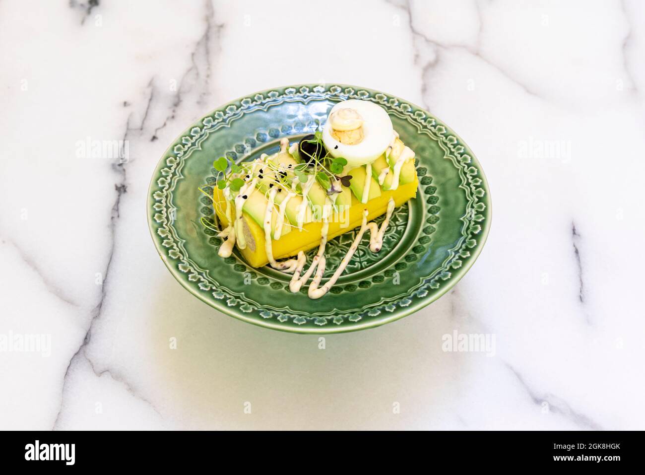 ricetta sofisticata adattata da causa limeña con avocado, uova sode, olive nere, germogli e maionese su un bellissimo piatto verde e marb bianco Foto Stock