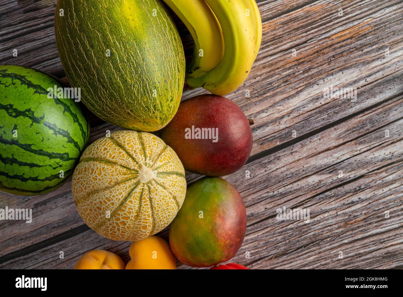 Immagine dall'alto di manga africane mature, meloni europei e anguria, banane delle canarie e pesche gialle sul tavolo di legno. Foto Stock