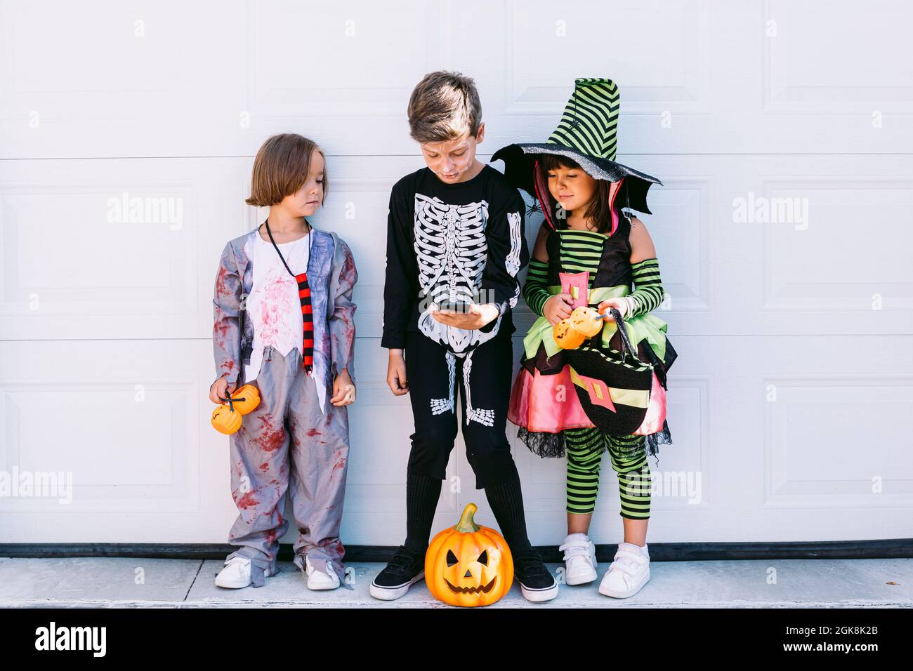 Corpo pieno di gruppo di bambini piccoli vestiti in vari costumi di  Halloween con scolpito Jack o Lantern navigare telefono cellulare insieme  mentre si piedi vicino Foto stock - Alamy