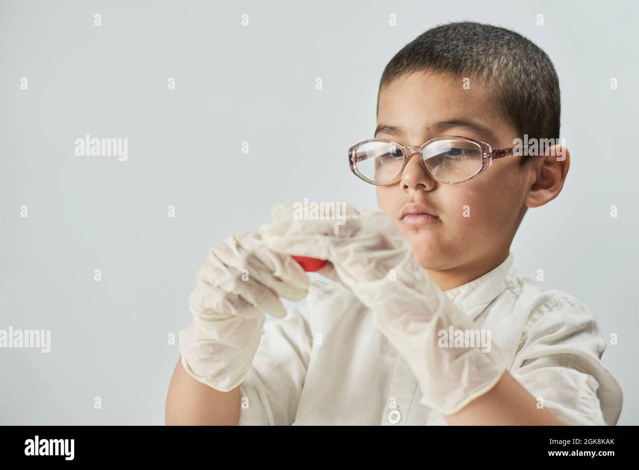 Un ritratto di ragazzo carino in guanti e occhiali protettivi che fanno figurine di plastilina sul tavolo Foto Stock