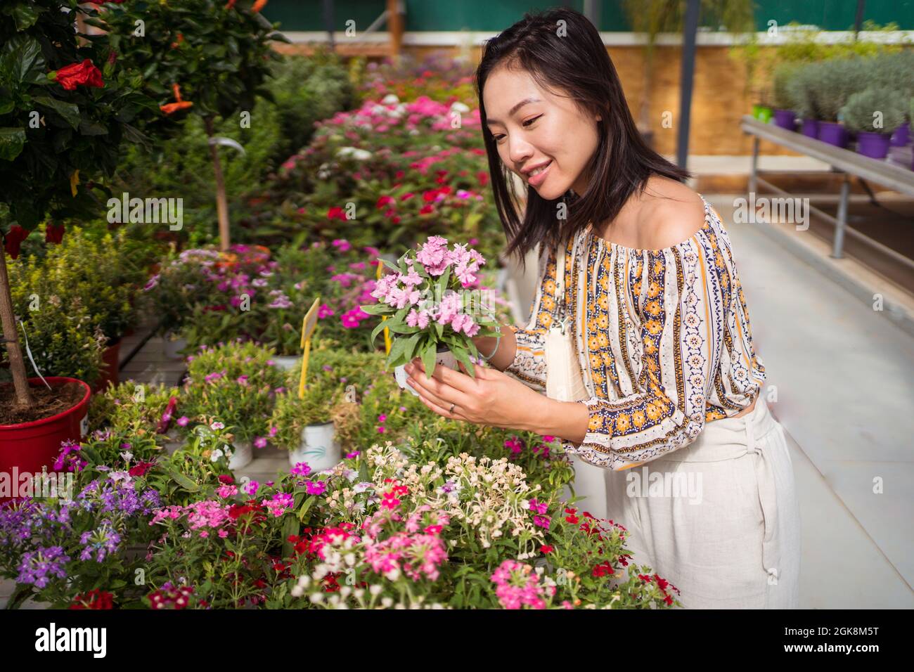 Sincera giovane etnia shopper selezionare fiori in fiore con profumo piacevole in negozio giardino di giorno Foto Stock