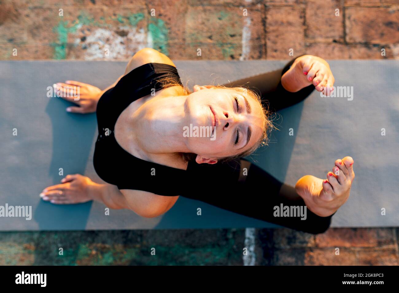 Giovane donna snella in abbigliamento sportivo facendo Raja Bhujangasana mentre pratica yoga in città in giorno di sole Foto Stock