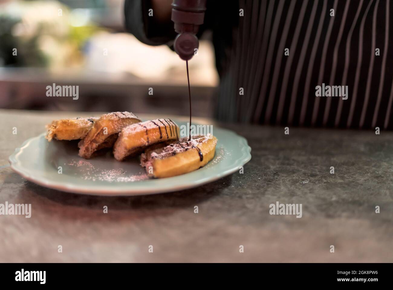 Raccolto irriconoscibile cuoco maschile decorazione deliziosi waffle viennesi con salsa di cioccolato da bottiglia in cucina ristorante Foto Stock