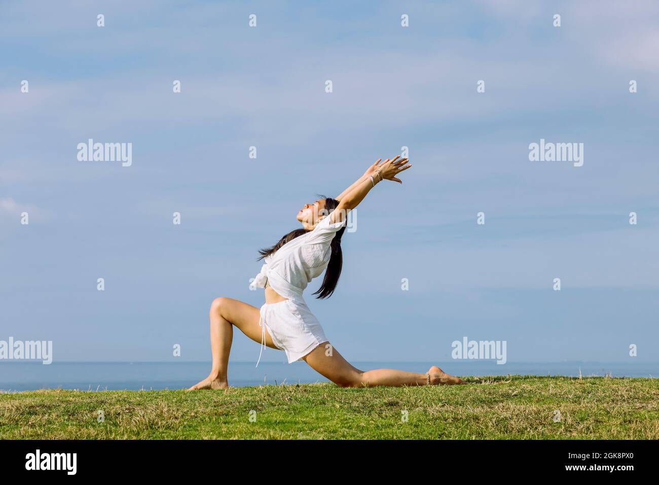 Vista laterale della giovane etnia femminile in abbigliamento sportivo in piedi ad Ashta Chandrasana posa durante la pratica di yoga sulla riva del mare Foto Stock
