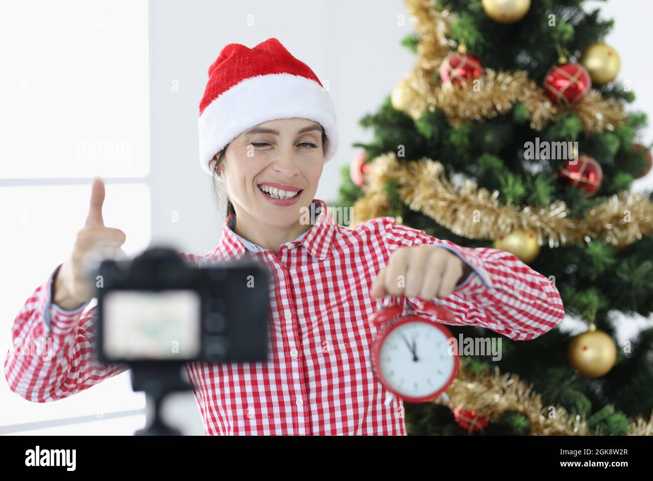 Giovane donna blogger in babbo natale cappello tiene sveglia e verricelli alla macchina fotografica Foto Stock