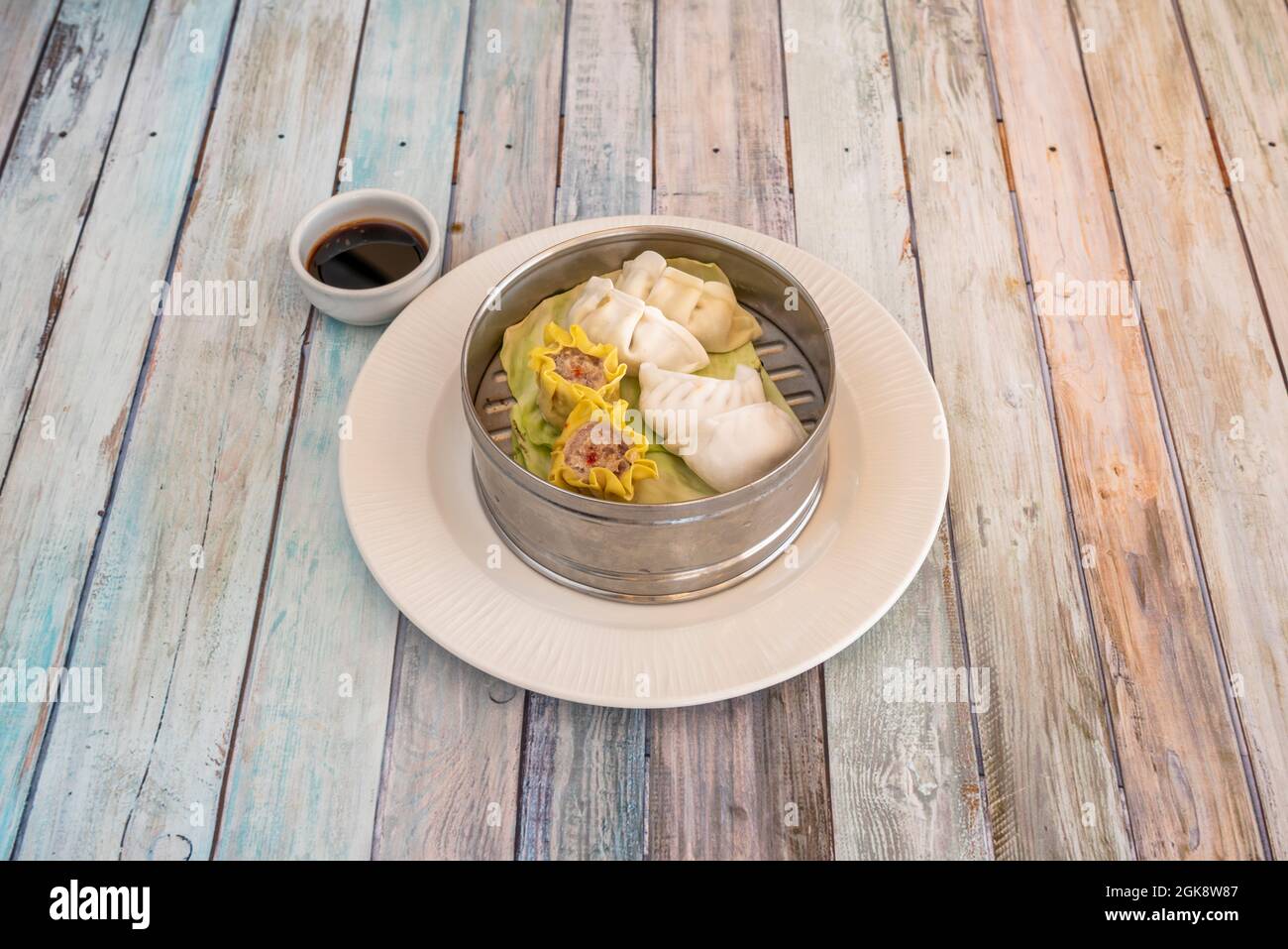 Dim sum e gyozas assortiti al vapore in una ciotola di acciaio inossidabile con salsa di soia per l'immersione cucinata da uno chef cinese Foto Stock