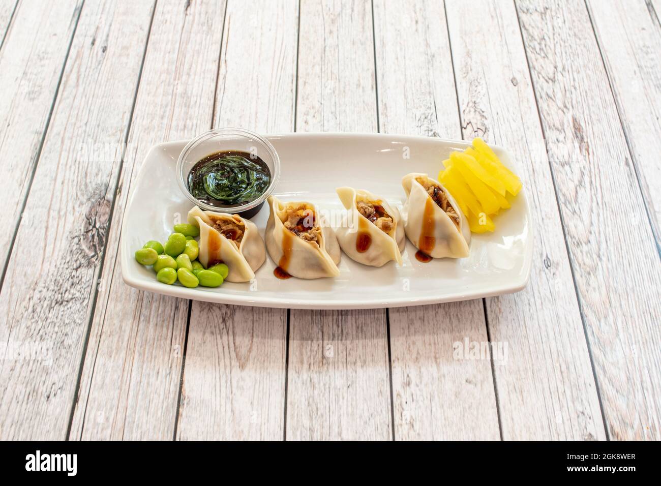 Vassoio di gnocchi ripieni di carne con salsa di soia, peperoni gialli grattugiati e fagioli edamame Foto Stock