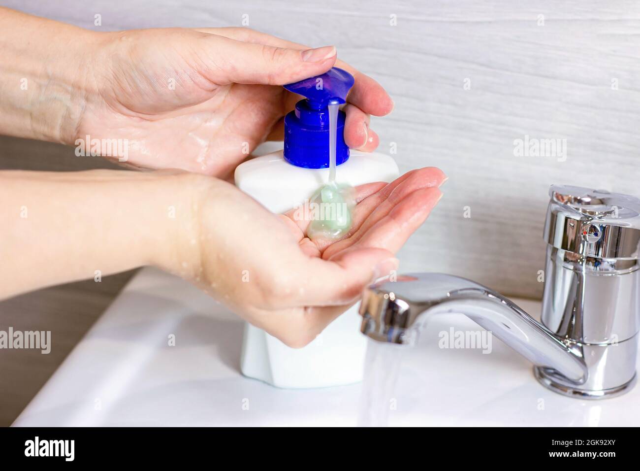 La giovane donna caucasica lava le mani con acqua e sapone antisettico liquido in bagno. Foto Stock
