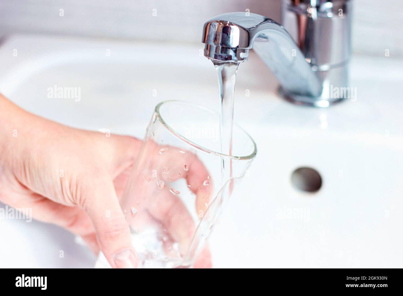 Giovane donna caucasica mano tenendo un bicchiere con acqua potabile pura versando da casa rubinetto primo piano. Foto Stock