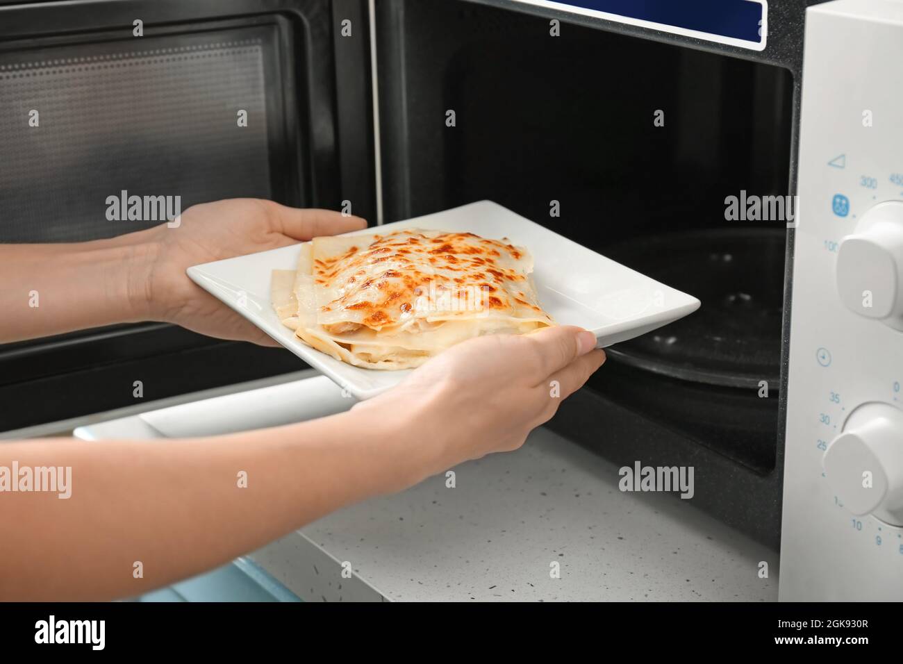 Donna di mettere la piastra di lasagne nel forno a microonde in cucina Foto  stock - Alamy
