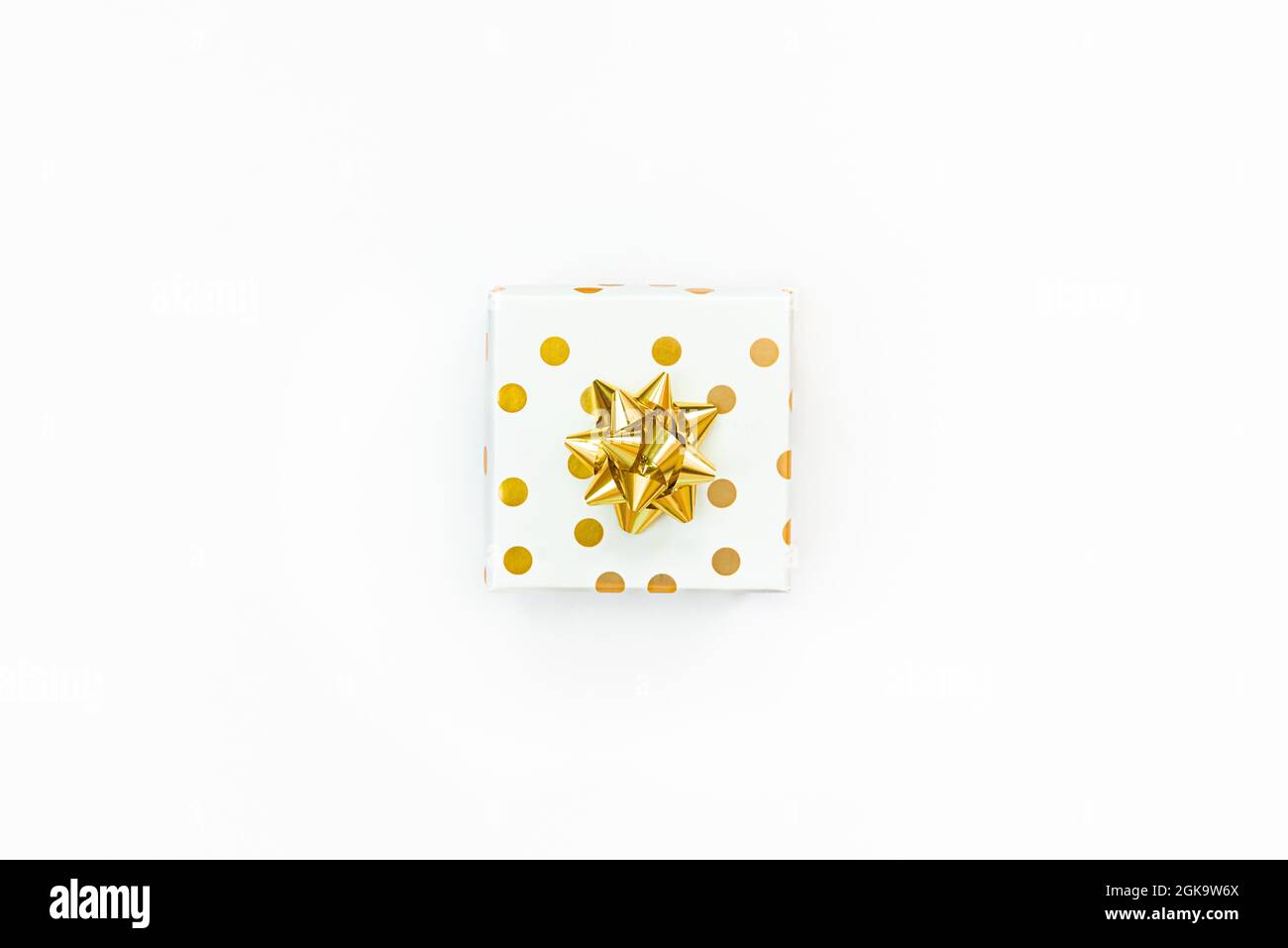 Vista dall'alto di una confezione regalo punteggiata d'oro su sfondo bianco. Foto Stock