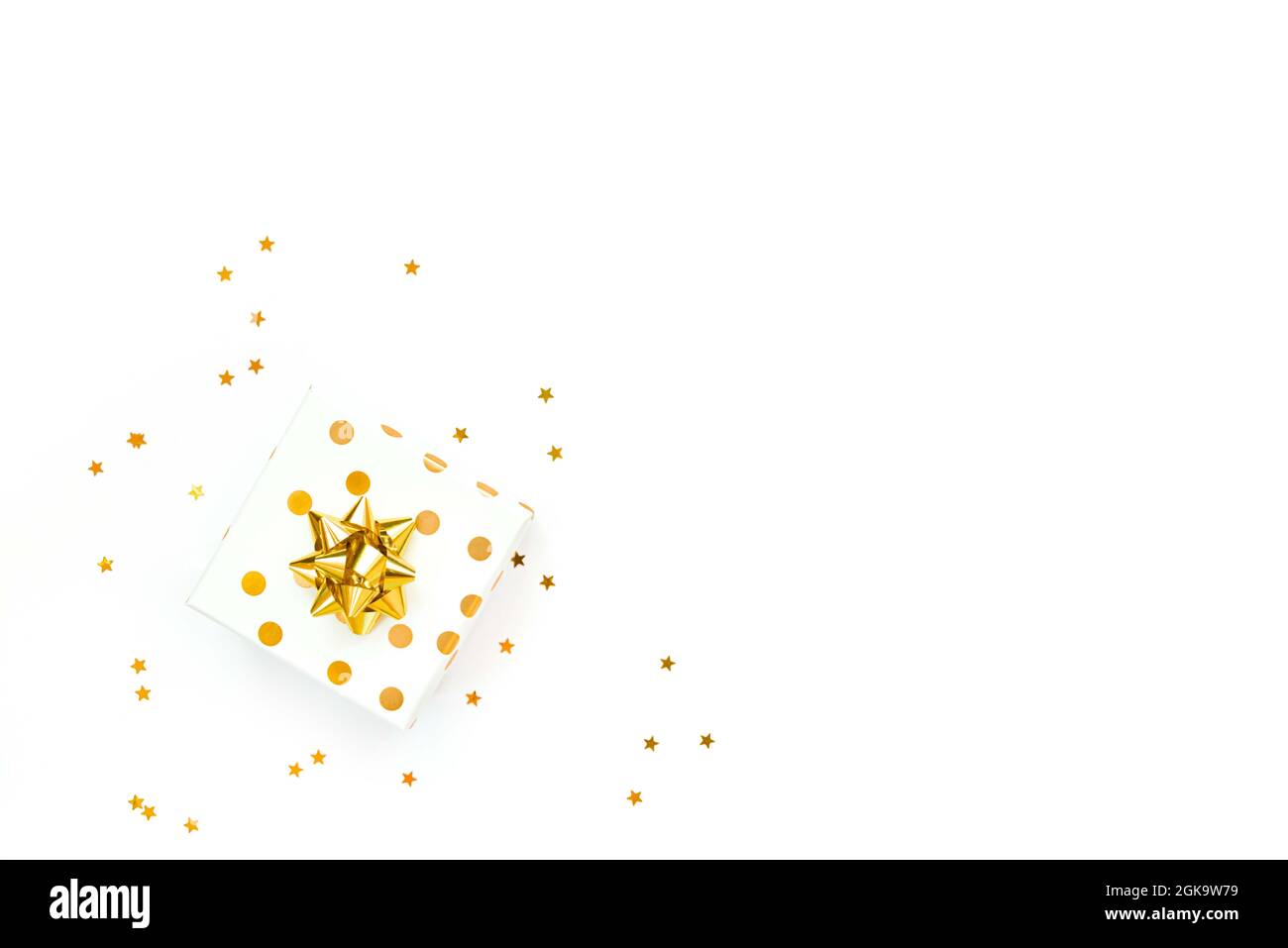 Vista dall'alto di una scatola regalo punteggiata d'oro e di un confetto dorato a forma di stella su sfondo bianco. Spazio di copia. Foto Stock
