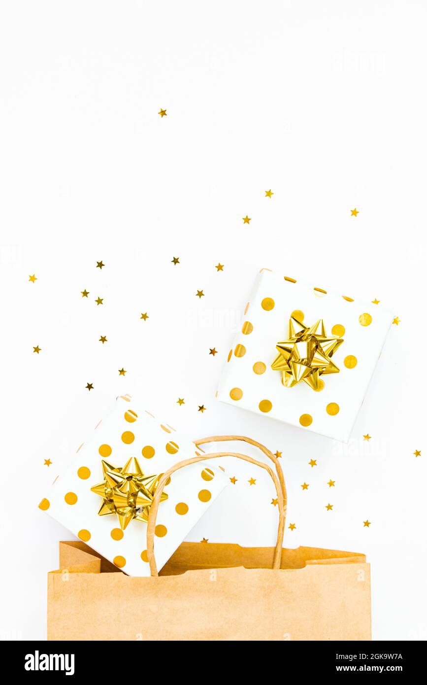 Vista dall'alto delle confezioni regalo punteggiate d'oro, una borsa per la spesa e dei confetti dorati a forma di stella su sfondo bianco. Spazio di copia. Foto Stock