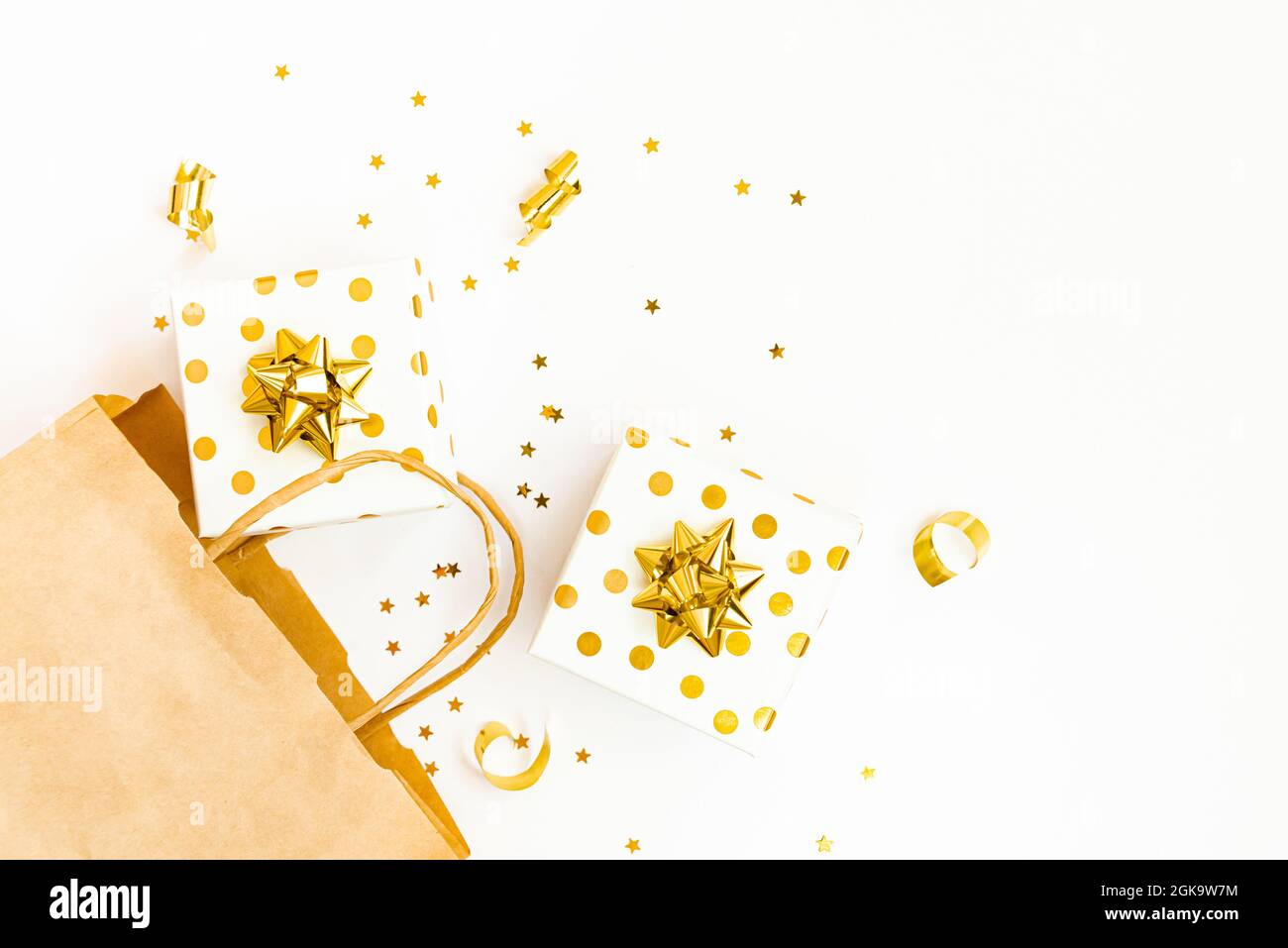 Vista dall'alto delle confezioni regalo punteggiate d'oro, una borsa per la spesa e dei confetti dorati a forma di stella su sfondo bianco. Spazio di copia. Foto Stock