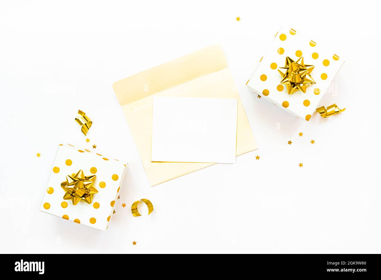 Vista dall'alto delle confezioni regalo punteggiate d'oro e busta aperta con carta vuota su sfondo bianco. Spazio copia, mock-up. Foto Stock