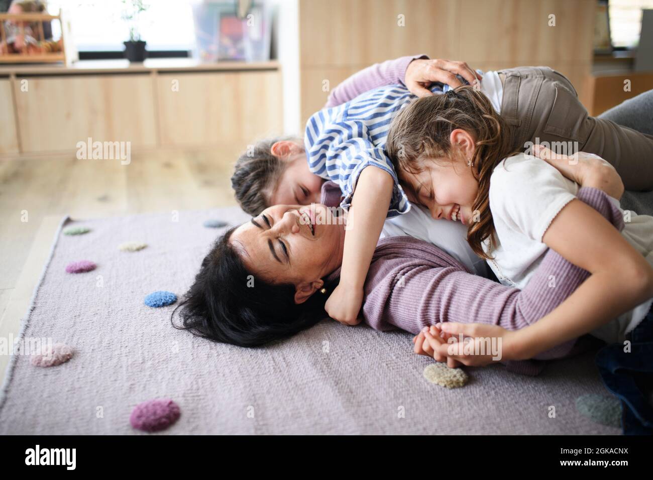 Ragazze piccole felici con nonna anziana al coperto a casa, giocando sul pavimento. Foto Stock