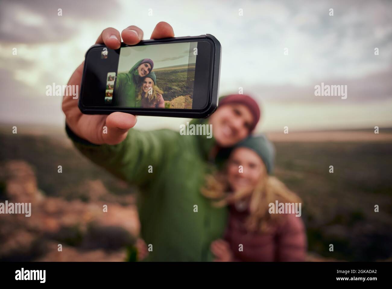 Primo piano di mano maschile che tiene smartphone prendere selfie con la ragazza mentre sulla collina di montagna dopo l'escursione Foto Stock