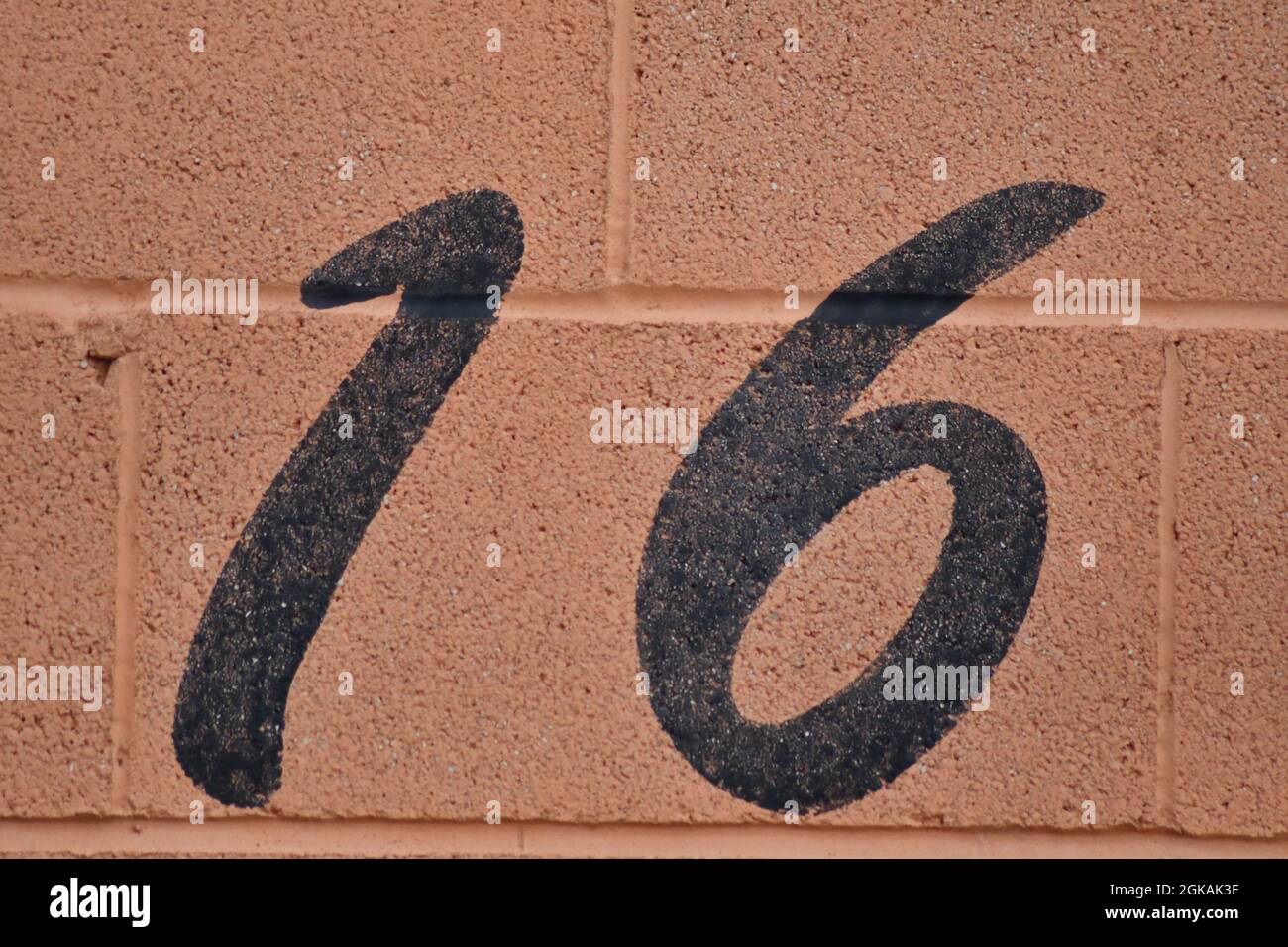 Un numero nero 16, sedici, dipinto in nero su una parete di blocco arancione all'esterno di un garage auto da corsa Foto Stock