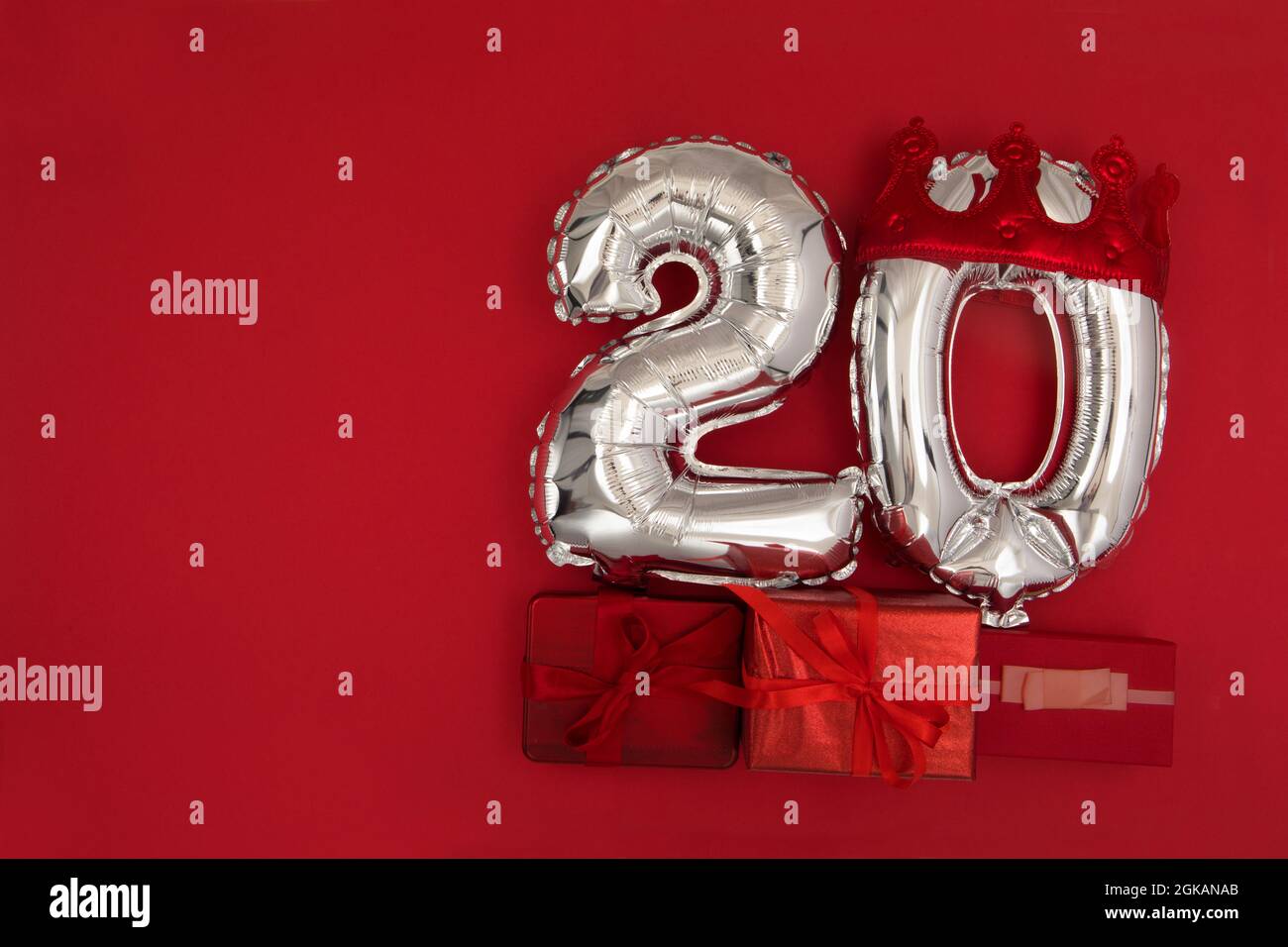 Palloncini d'aria in lamina d'argento che mostrano il numero 20 venti posti su sfondo rosso con i regali avvolti per il concetto di anniversario di compleanno Foto Stock