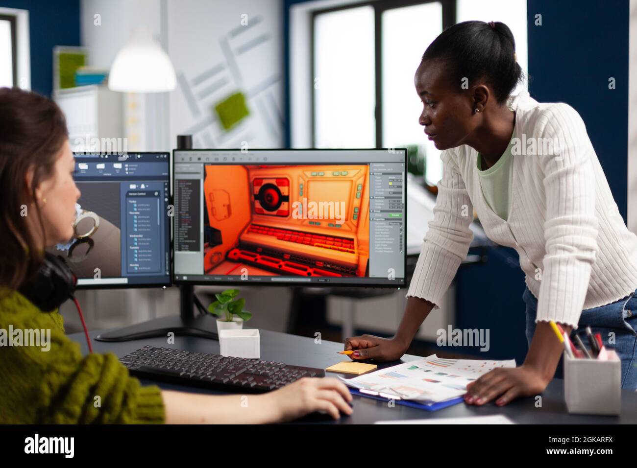 Designer multietnico che guarda computer con doppio display che lavorano insieme al progetto di gioco in startup Office. Lavoratori dei videogamer che sviluppano videogiochi digitali su pc con tecnologia moderna Foto Stock