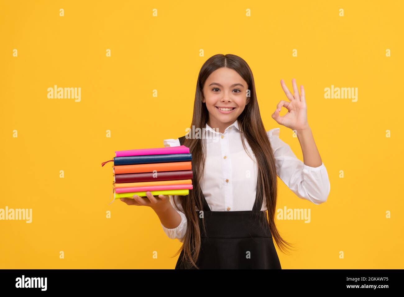 ragazzo bookish nella scuola di grammatica. ragazza teen felice tiene i libri heap. istruzione perfetta Foto Stock