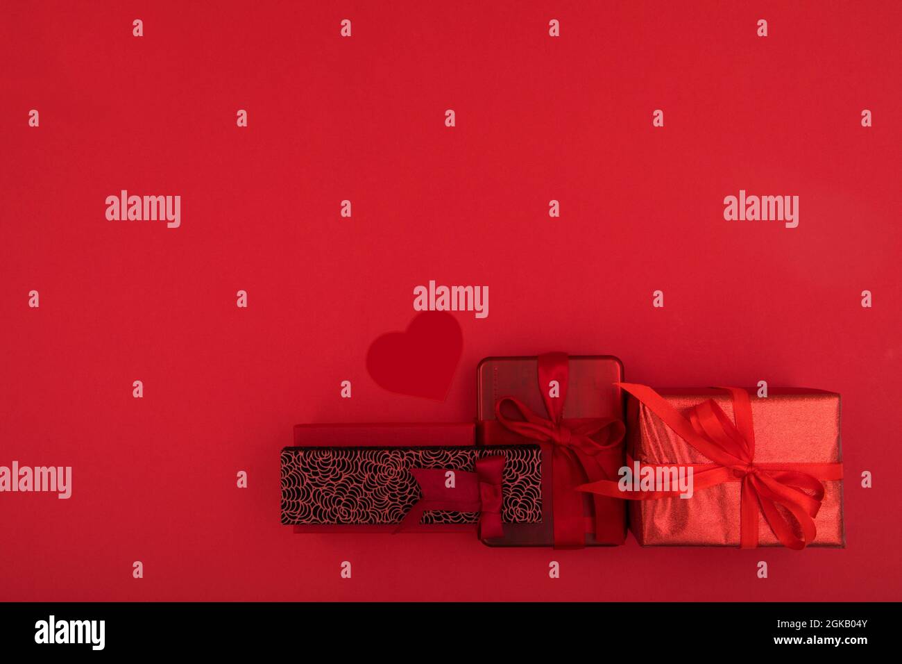 Vista dall'alto composizione di vari regali natalizi avvolta in carta con nastri e sfere decorative poste su una superficie rossa brillante con spazio vuoto Foto Stock