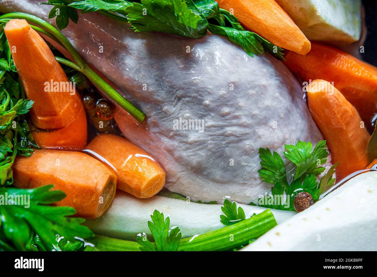 Zuppa di pollo tradizionale e lucidata (brodo) prima della cottura. Primo piano - su ingredienti crudi: Pollo, carote, sedano e prezzemolo in acqua. Pasto sano. Foto Stock