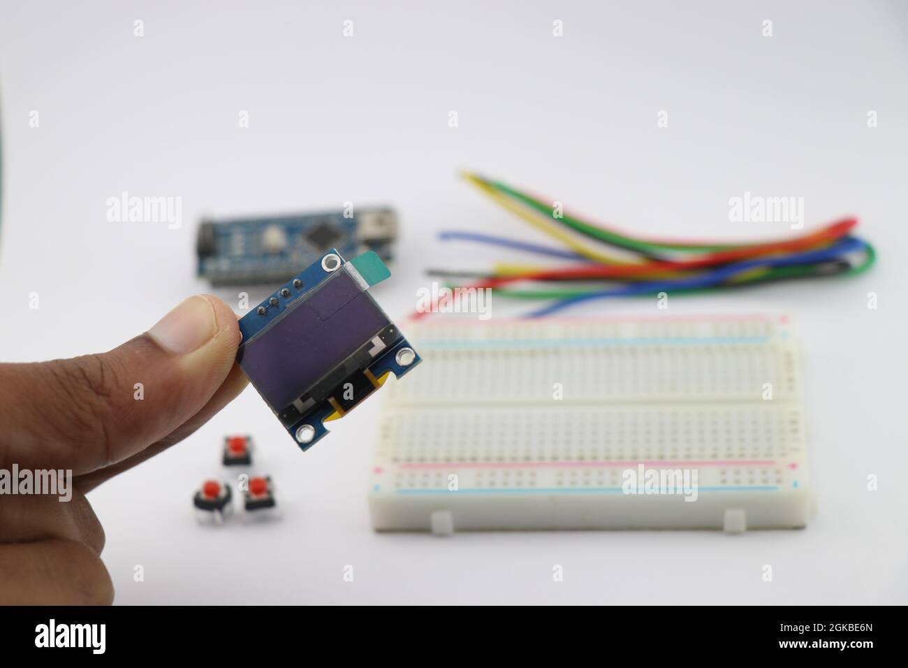 Giovane inventore che tiene in mano il display OLED, modulo display Arduino con breadboard e fili sullo sfondo che mostra progetti elettronici creativi Foto Stock