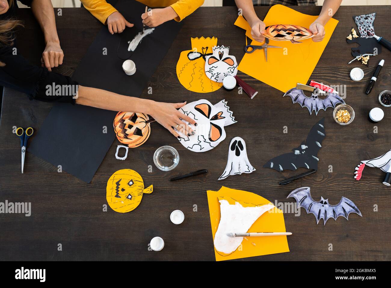 Mani di bambini e giovane donna che dipingono simboli di carta di Halloween insieme da tavolo Foto Stock