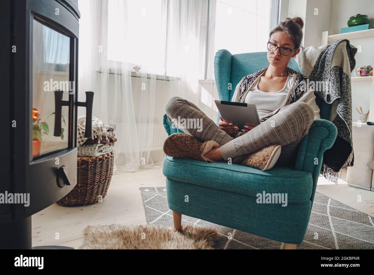 donna accanto al camino, seduta in una comoda poltrona, con un caldo Foto Stock