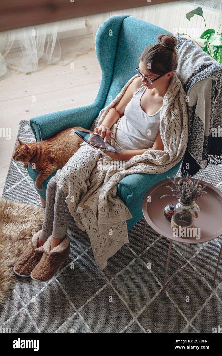 donna seduta in comoda poltrona, con coperta calda, con tablet Foto Stock