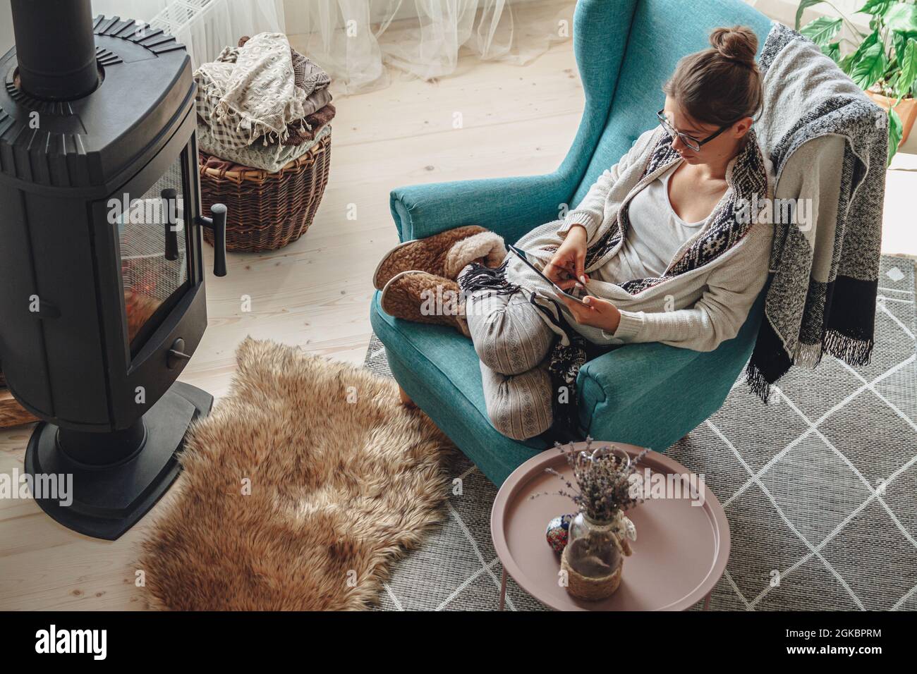 donna accanto al camino, seduta in una comoda poltrona, con un caldo Foto Stock
