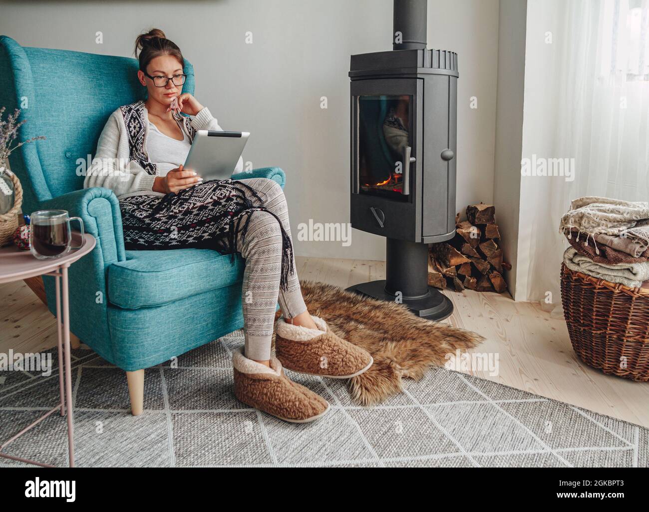 donna accanto al camino, seduta in una comoda poltrona, con un caldo Foto Stock