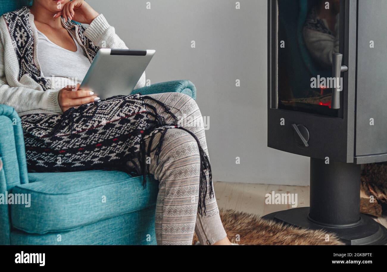 donna accanto al camino, seduta in una comoda poltrona, con un caldo Foto Stock