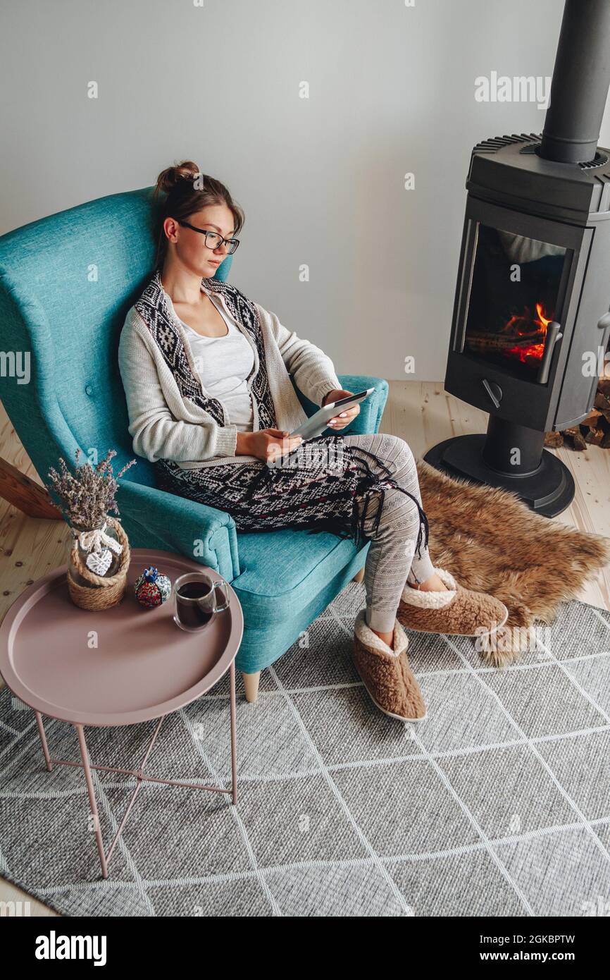 donna accanto al camino, seduta in una comoda poltrona, con un caldo Foto Stock