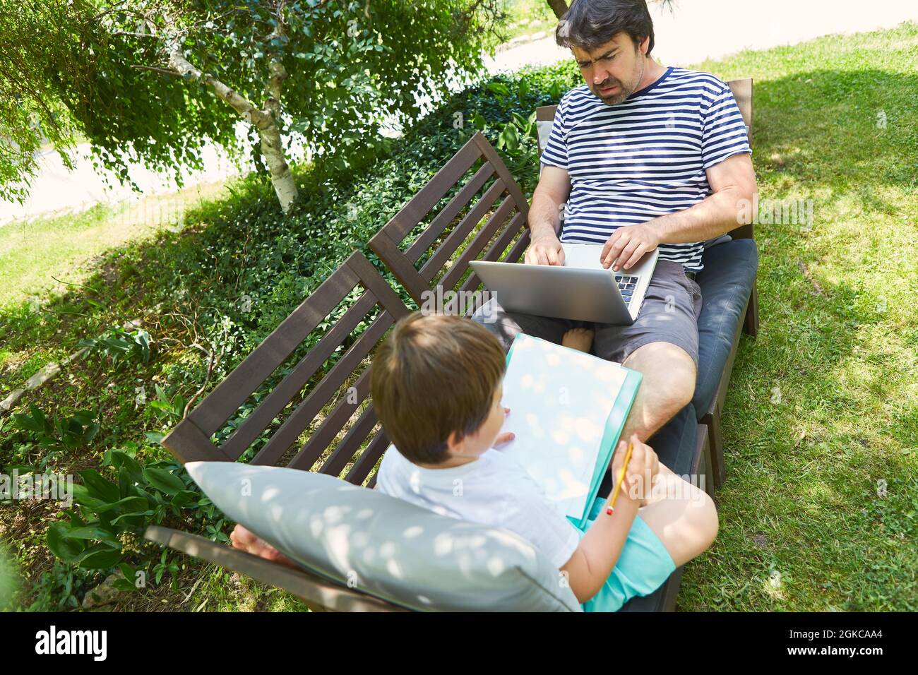 Bambino che fa i compiti in giardino in estate con il padre sul computer portatile Foto Stock