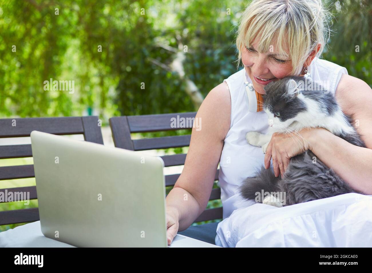 Donna con gatto sul PC portatile durante la riunione di video chat zoom durante il tempo libero in giardino Foto Stock