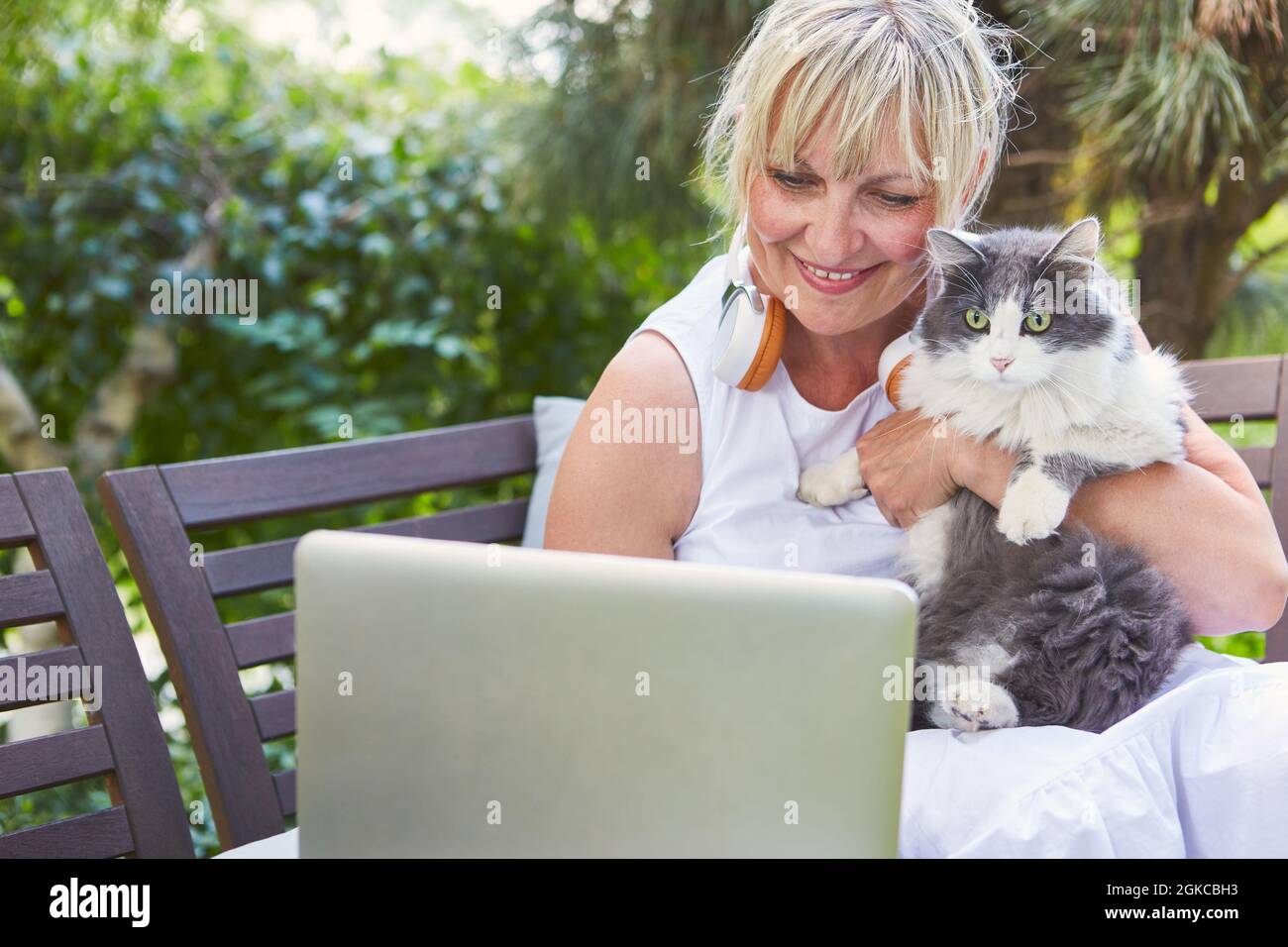 Donna anziana con gatto durante la video chat sul PC portatile in giardino in vacanza in estate Foto Stock