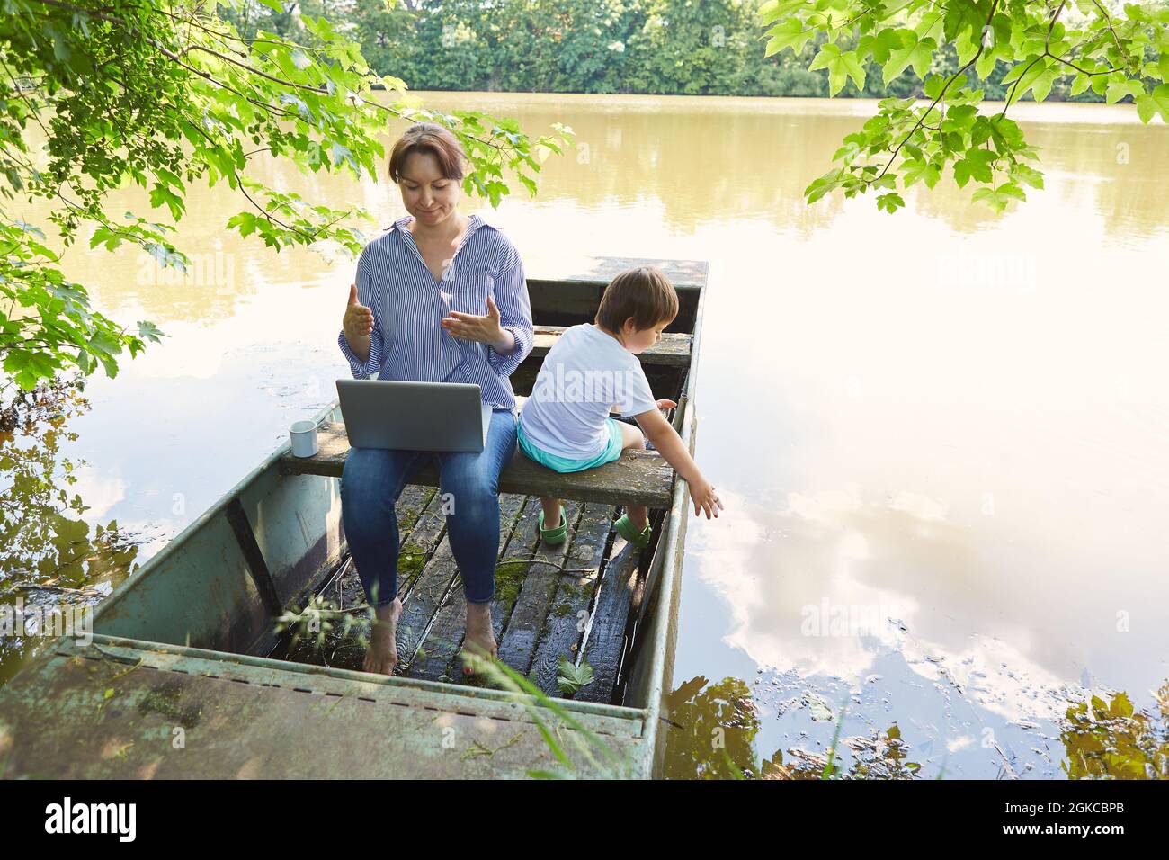 Madre singola che usa il computer portatile al lago in estate con figlio con lei Foto Stock